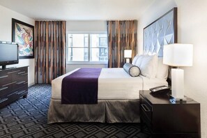 A hotel room with a bed, a TV, a desk, a lamp, and a window with curtains. - Miami Beach 2BR | Beachfront Pool Retreat (Surfside)