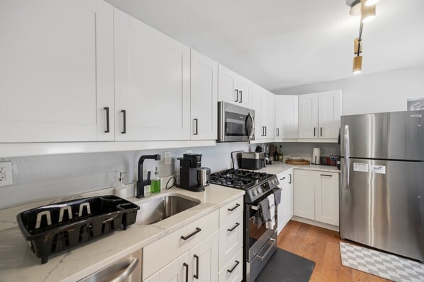 A modern kitchen with white cabinets, a stainless steel refrigerator, a microwave, a stove, and a sink.