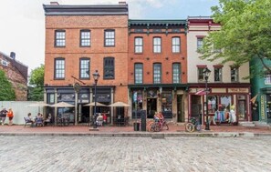 A row of brick buildings with outdoor seating, a bicycle, and a storefront with a sign.