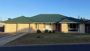 Um edifício térreo com telhado verde, garagem e um pequeno jardim frontal com plantas.