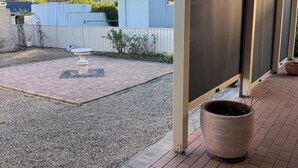 Uma área de pátio coberta com piso de cascalho, cerca branca e um grande jardim.