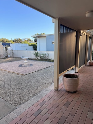 A covered patio area with a gravel floor, a white fence, and a large planter.