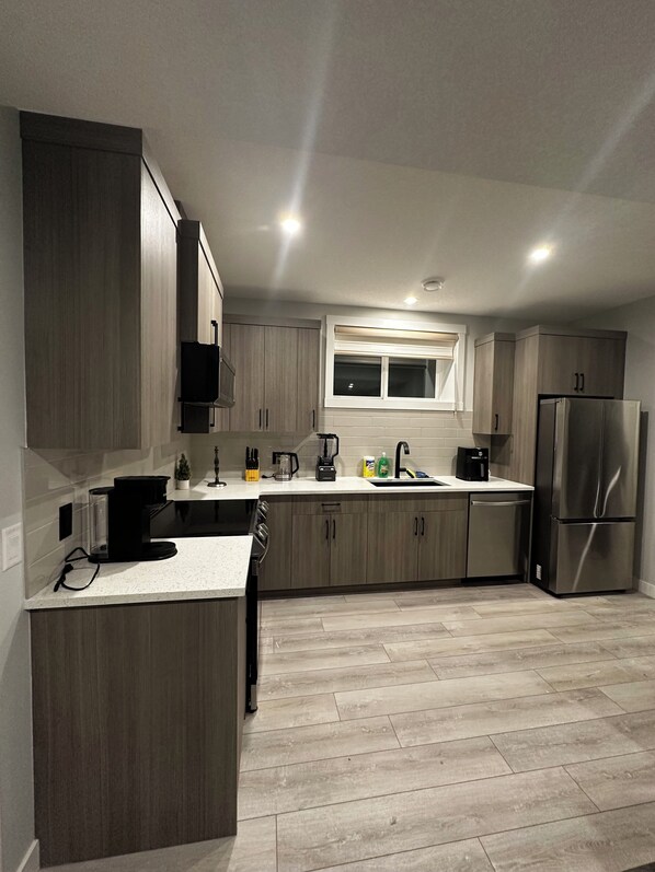 A modern kitchen with wooden cabinets, a stainless steel refrigerator, and a window above the sink.