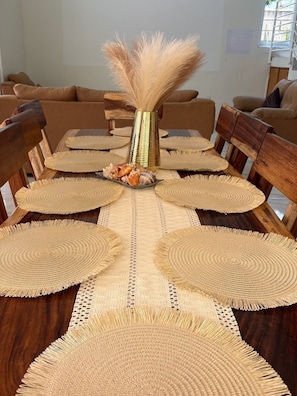 A dining table with woven placemats, a decorative vase with dried plants, and a wooden chair. - Cocos House Zicatela (Brisas de Zicatela)