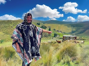 A person standing in a grassy field with a mountainous landscape in the background.