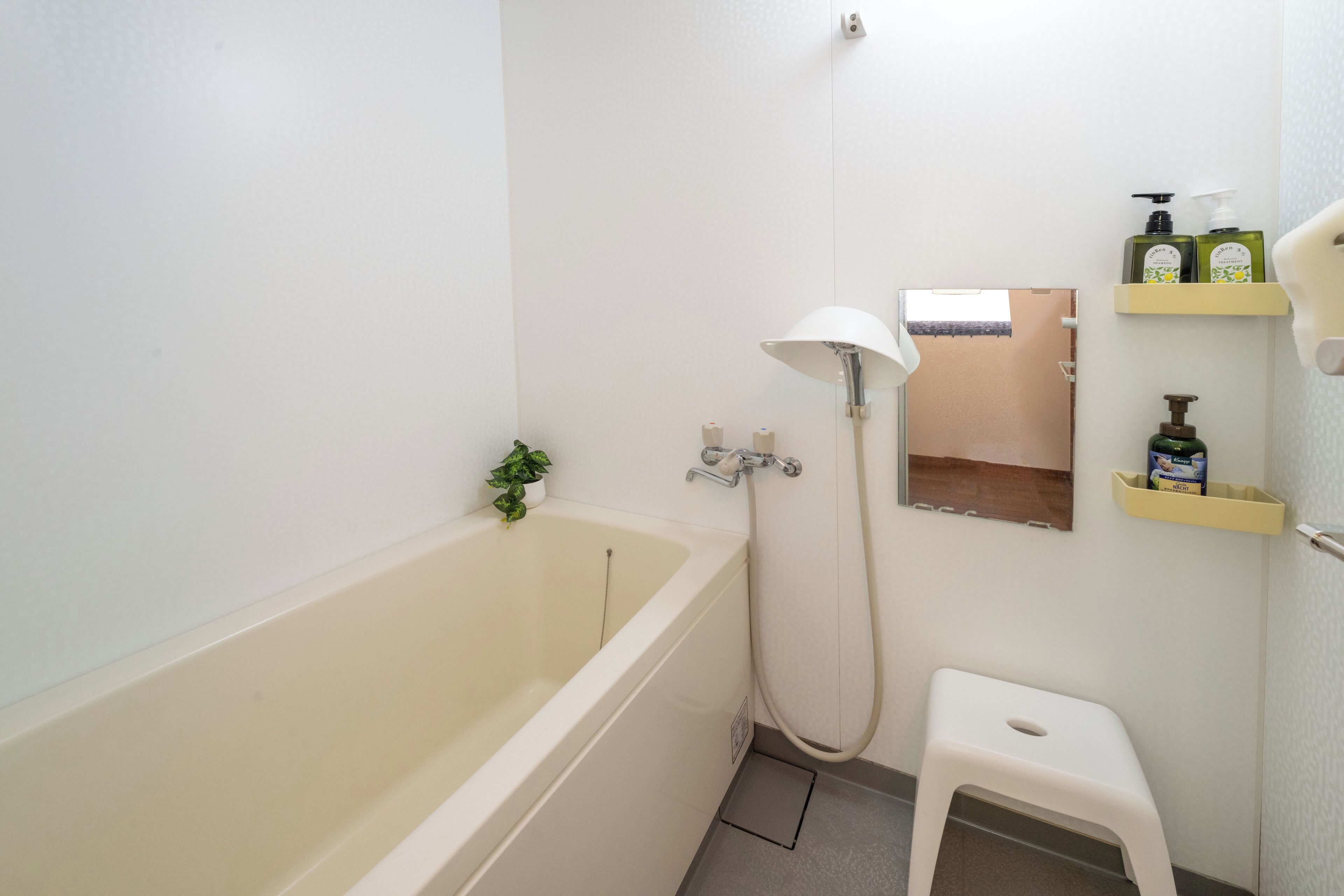 A bathroom with a bathtub, a shower, a small stool, and shelves with toiletries.