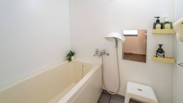 A bathroom with a bathtub, a shower, a small stool, and shelves with toiletries.