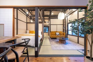 A traditional Japanese-style room with tatami flooring, a bed, a sofa, a table, and a potted plant.