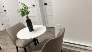 Un'area pranzo con un tavolo rotondo, due sedie, un vaso con una pianta e una porta sullo sfondo.