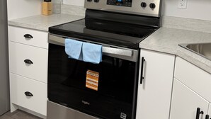Una cucina con microonde in acciaio inossidabile, forno e lavastoviglie, mobili bianchi e un piano di lavoro.