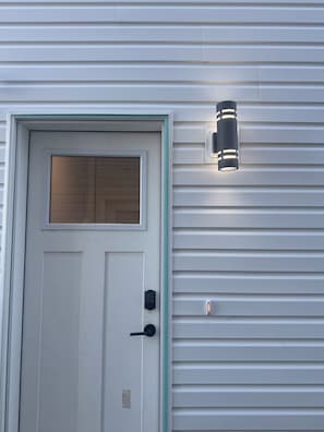 Une porte blanche avec une fenêtre, un clavier pour ouvrir la porte et un luminaire fixé au mur.