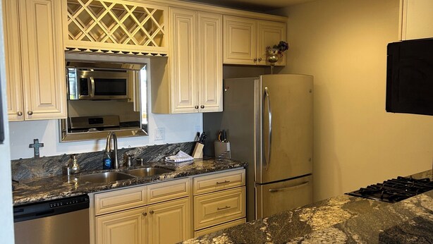 A kitchen with white cabinets, a stainless steel refrigerator, a microwave, and a granite countertop. - Huntington Beach Condo (Huntington Beach)