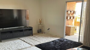 A bedroom with a bed, a glass table, a TV, a ceiling fan, and a view of the outside. - Huntington Beach Condo (Huntington Beach)