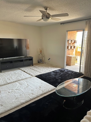 A bedroom with a bed, a TV, a ceiling fan, a glass table, and a view of the outside. - Huntington Beach Condo (Huntington Beach)