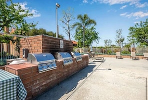 A barbecue grill with multiple burners, a brick wall, and outdoor seating. - Huntington Beach Condo (Huntington Beach)