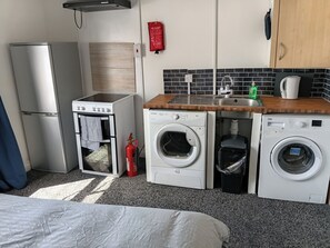 A compact kitchenette with a refrigerator, oven, microwave, and washing machine. - Studio Sleeps 2 with Parking (Oldbury)