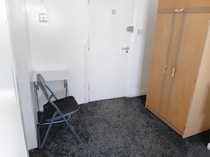 A room with a white door, a wooden wardrobe, a folding chair, and a carpeted floor. - Studio Sleeps 2 with Parking (Oldbury)