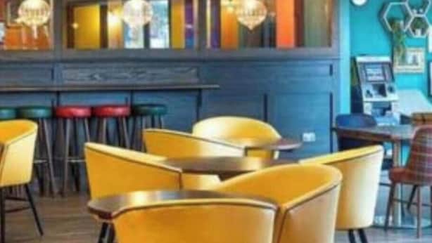 Un interior de restaurante con sillas amarillas, una zona de bar y una pared azul con decoraciones hexagonales.