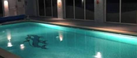 An indoor swimming pool with a clear water surface, a diving board, and a tiled floor.