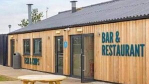 Un edificio de madera con un letrero que dice 'BAR & RESTAURANT' y una mesa de picnic afuera.