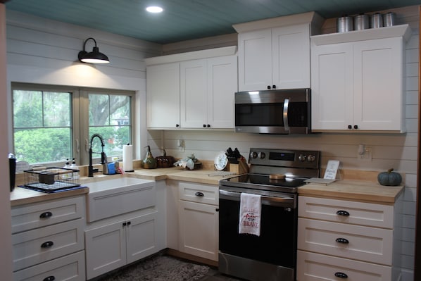 A kitchen with white cabinets, a stainless steel oven, a microwave, and a window with a view of greenery.