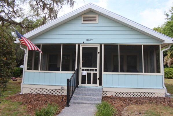 A light blue building with a number '20920' above the door, a porch with a black railing, and an American flag to the left.