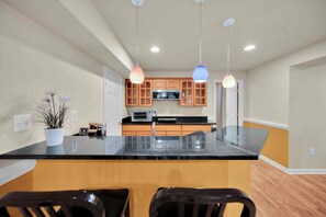A modern kitchen with a central island, wooden cabinets, and pendant lighting. - Modern Basement Suit of Fairfax (Fairfax)