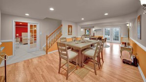 A spacious dining area with a wooden table and chairs, a staircase, and a view of a balcony.