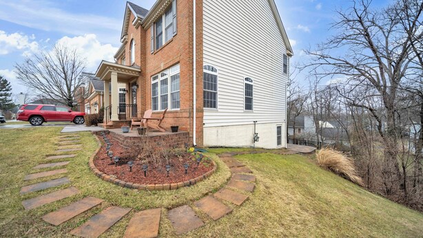 A two-story house with a brick facade and white siding, a front yard with a stone pathway, and a red SUV parked in the driveway.
