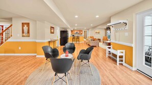 A spacious living area with a wooden floor, a dining table with chairs, a sofa, and a kitchen in the background.