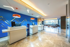 Un área de recepción moderna con un diseño geométrico azul y dorado en la pared, suelo de mármol pulido y dos lámparas colgantes naranjas.