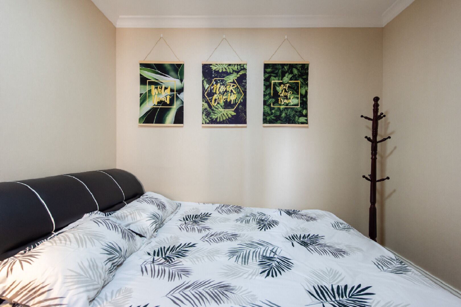 A bedroom with a bed, a coat rack, and three framed wall art pieces.