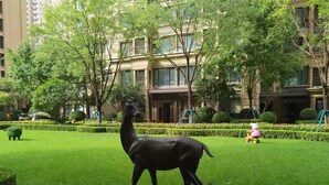 A well-maintained grassy area with a giraffe statue, surrounded by trees and a building with multiple windows.