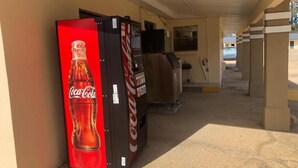 Un pasillo con una máquina expendedora de Coca-Cola y un televisor sobre un soporte.