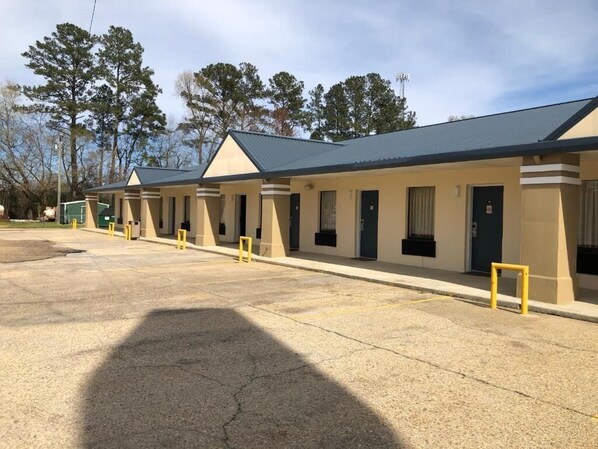 A motel with a row of rooms, each with a door and windows, and a parking lot in front. - Liberty Inn (Collins)