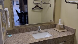 Un baño de hotel con encimera de granito, un lavamanos, un espejo, un secador de pelo, un perchero para toallas y un secador de manos.