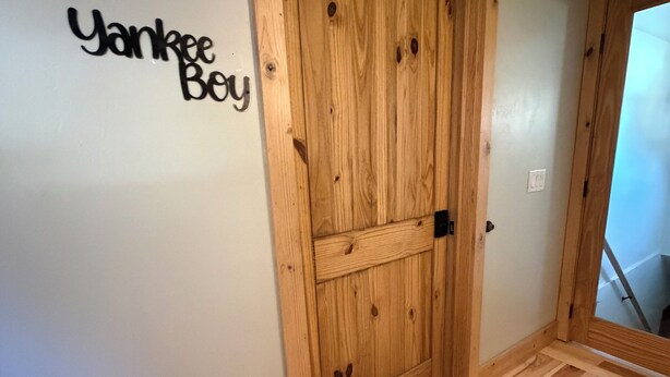 Eine Holztür mit Fußmatte, ein Schild mit der Aufschrift 'Yankee Boy' an der Wand und ein Holzboden.