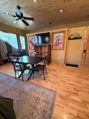 A dining area with a wooden table and chairs, a ceiling fan, and a mounted television. - Yankee Boy! Main Street with A/C and soaking Tub (Ouray)