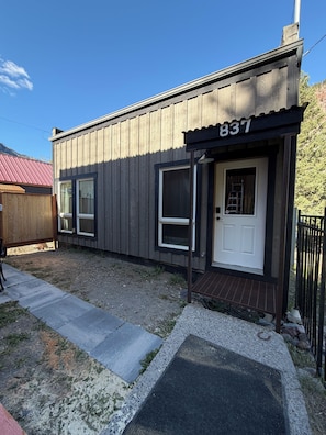 A small building with a number '837' above the door, a window, and a door with a small porch area. - Yankee Boy! Main Street with A/C and soaking Tub (Ouray)