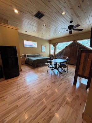 A cozy cabin interior with a wooden floor, a bed, a dining table with chairs, a ceiling fan, and a stone wall. - Yankee Boy! Main Street with A/C and soaking Tub (Ouray)
