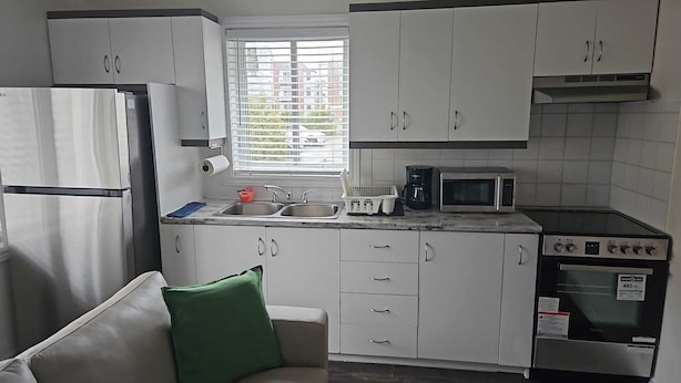 A compact kitchen with white cabinets, a stainless steel refrigerator, a microwave, a coffee maker, and a stove.