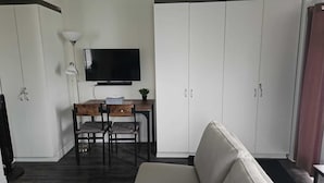 A room with a TV, a desk, two chairs, a sofa, and white wardrobes.