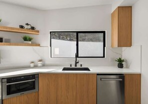 Eine moderne Küche mit Holzausstattung, einem eingebauten Ofen, einer Spülmaschine und einem Fenster über der Spüle.