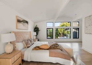 A spacious bedroom with a large bed, a nightstand, a lamp, and a window with a view of greenery. - Near LA Hollywood Garaged Parking Fast WiFi Pool (Los Angeles)