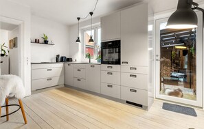 Eine moderne Küche mit weißen Schränken, einem schwarzen Kühlschrank und einem großen Fenster.