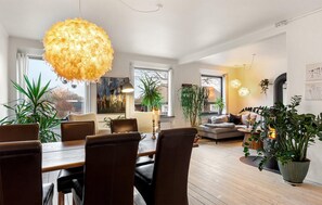 Ein modernes Wohnzimmer mit Essbereich, großen Fenstern und Zimmerpflanzen.