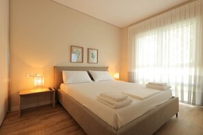 A hotel room with a large bed, bedside lamps, a nightstand, and a window with sheer curtains. - Sanpietro Vacation Apartment 012 (Ishëm)