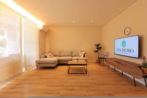 A modern living room with a sectional sofa, a coffee table, a TV mounted on the wall, and a wooden bench. - Sanpietro Vacation Apartment 012 (Ishëm)