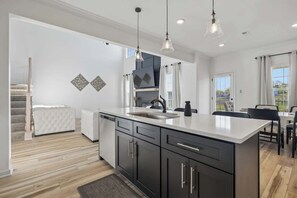 Une cuisine moderne dotée d’un grand îlot central, de meubles de rangement aux couleurs sombres et de luminaires suspendus.