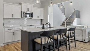 A modern kitchen with white cabinets, a central island with bar stools, a stainless steel microwave, and pendant lighting. - Fort Haven Near Fort Campbell, Spacious 4BR Retreat (Clarksville)